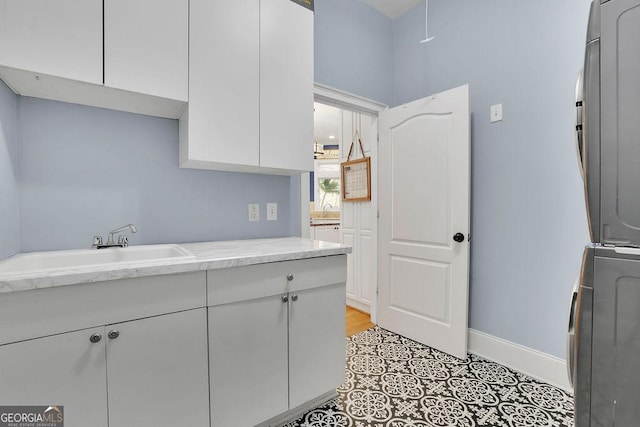 kitchen with white cabinets, light stone counters, sink, and stacked washer and clothes dryer