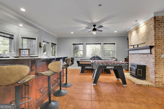 game room with a wood stove, ceiling fan, crown molding, and light tile patterned floors