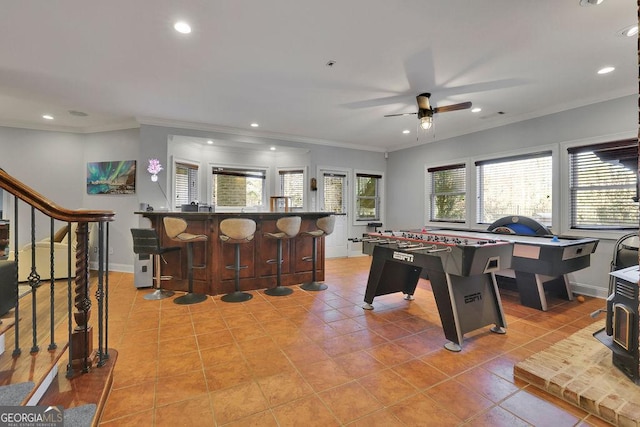 recreation room with bar area, ceiling fan, light tile patterned floors, and ornamental molding