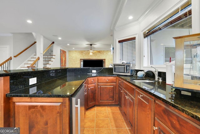 kitchen featuring sink, a brick fireplace, ceiling fan, dark stone countertops, and light tile patterned flooring