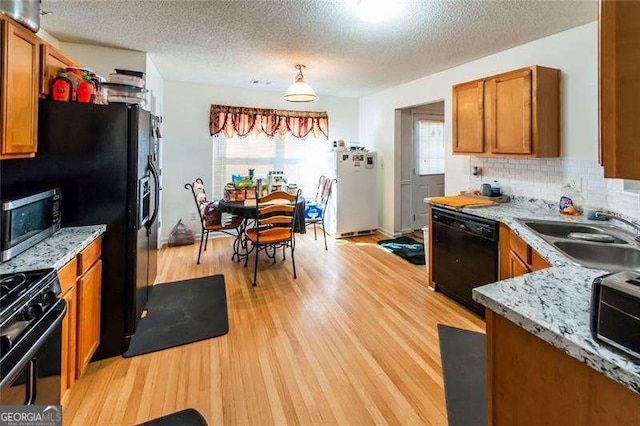 kitchen with sink, light stone counters, light hardwood / wood-style floors, decorative light fixtures, and black appliances