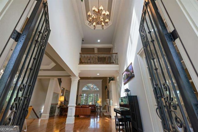 entrance foyer featuring ornate columns, a high ceiling, an inviting chandelier, dark hardwood / wood-style floors, and crown molding