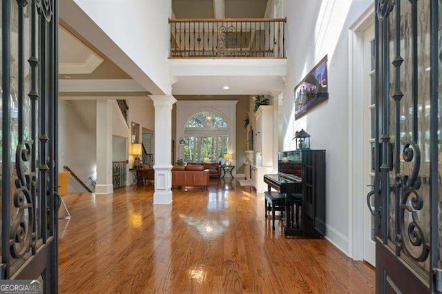 foyer featuring hardwood / wood-style floors, decorative columns, crown molding, and a high ceiling