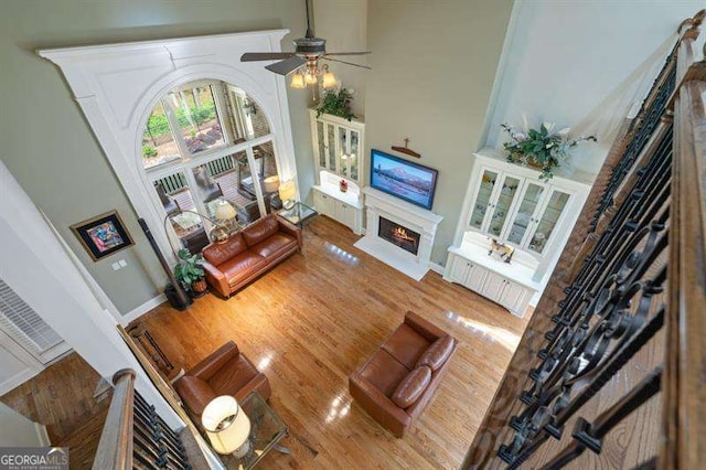 living room with ceiling fan, a towering ceiling, and wood-type flooring