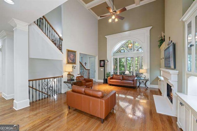 living room with beam ceiling, ceiling fan, coffered ceiling, a towering ceiling, and light hardwood / wood-style floors