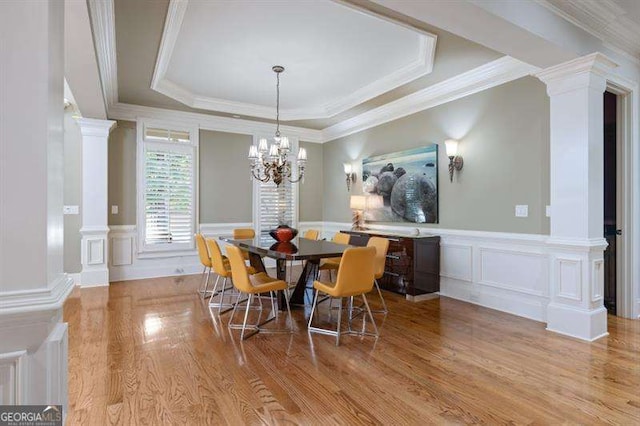 dining space with decorative columns, light hardwood / wood-style flooring, a tray ceiling, and crown molding