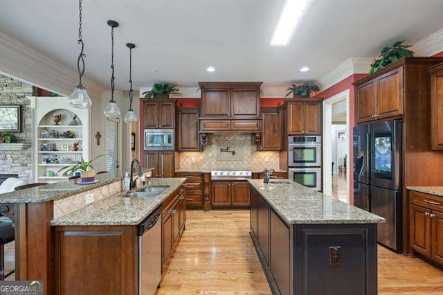 kitchen with sink, hanging light fixtures, stainless steel appliances, a large island with sink, and light hardwood / wood-style floors