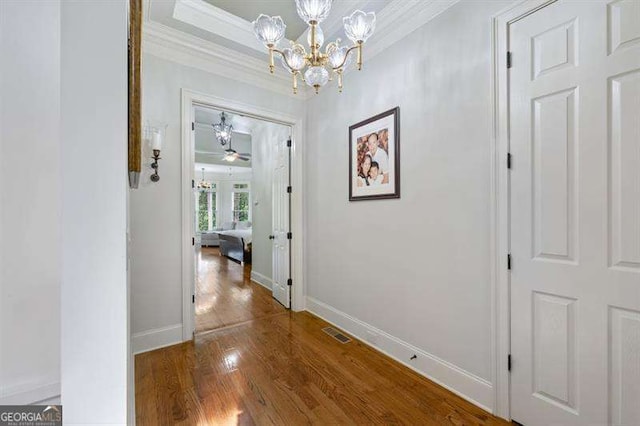 hall with hardwood / wood-style floors, crown molding, and an inviting chandelier