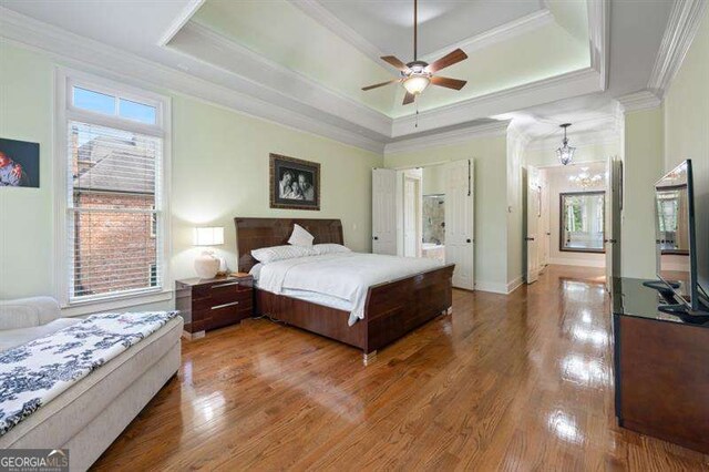 bedroom featuring ceiling fan with notable chandelier, hardwood / wood-style flooring, a raised ceiling, and ornamental molding