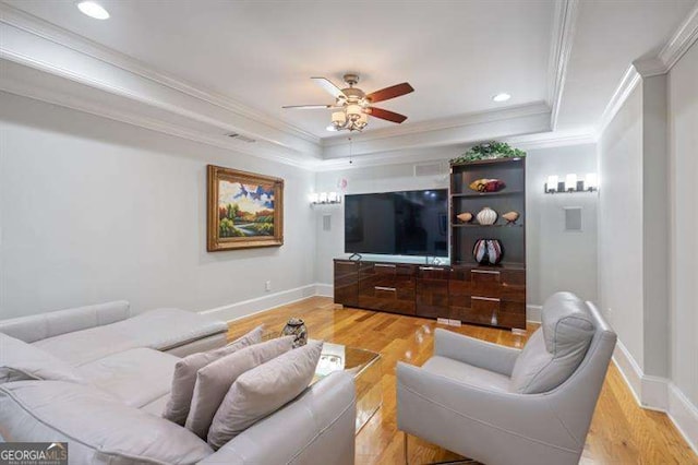 living room featuring ceiling fan, ornamental molding, a tray ceiling, and light hardwood / wood-style flooring