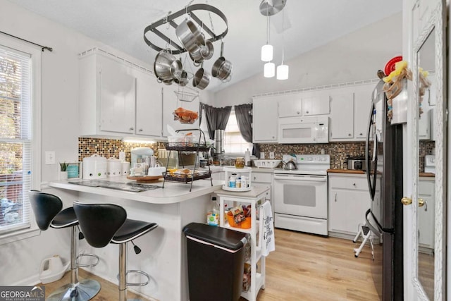 kitchen with kitchen peninsula, light hardwood / wood-style floors, lofted ceiling, white appliances, and white cabinets