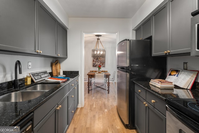 kitchen with gray cabinetry, sink, decorative light fixtures, dark stone countertops, and light hardwood / wood-style floors