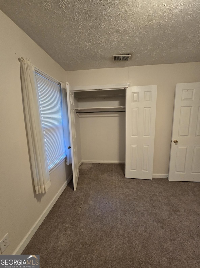 unfurnished bedroom featuring a closet, a textured ceiling, and dark colored carpet