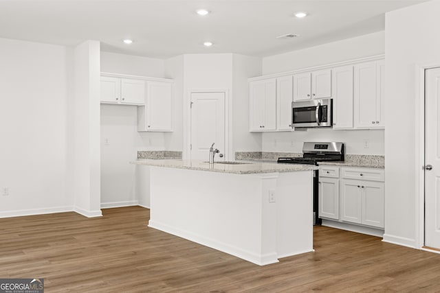 kitchen with white cabinetry, light stone countertops, hardwood / wood-style floors, a kitchen island with sink, and appliances with stainless steel finishes