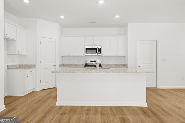 kitchen with a center island with sink, light wood-type flooring, appliances with stainless steel finishes, light stone counters, and white cabinetry