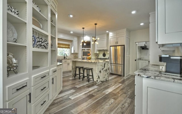 kitchen with dark wood-type flooring, light stone countertops, a kitchen island, white cabinetry, and stainless steel appliances