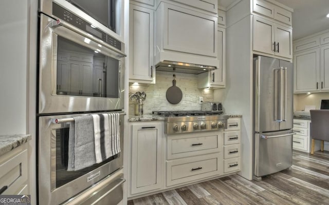 kitchen featuring dark hardwood / wood-style flooring, light stone counters, decorative backsplash, and appliances with stainless steel finishes