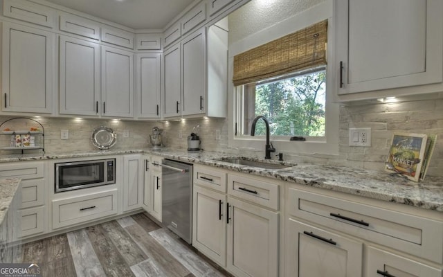 kitchen with white cabinetry, sink, light hardwood / wood-style flooring, decorative backsplash, and appliances with stainless steel finishes