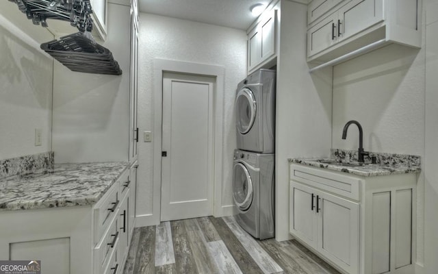 washroom featuring cabinets, sink, stacked washer and dryer, light wood-type flooring, and a textured ceiling