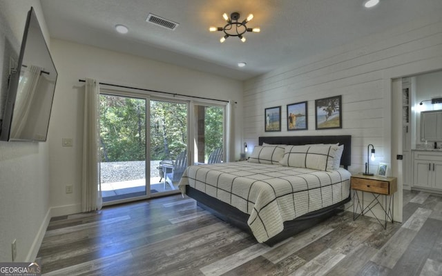 bedroom featuring ensuite bath, access to exterior, dark hardwood / wood-style floors, a notable chandelier, and wooden walls