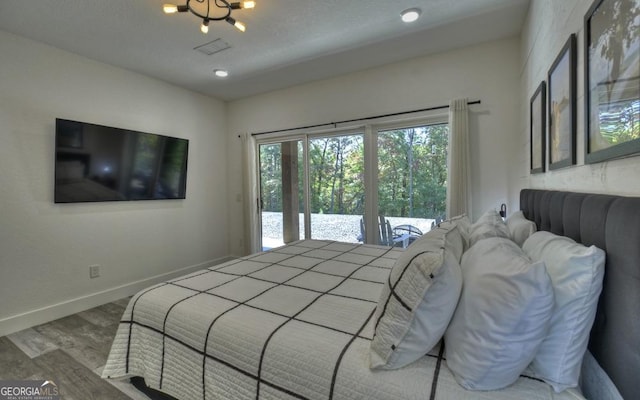 bedroom with access to outside, an inviting chandelier, and hardwood / wood-style flooring