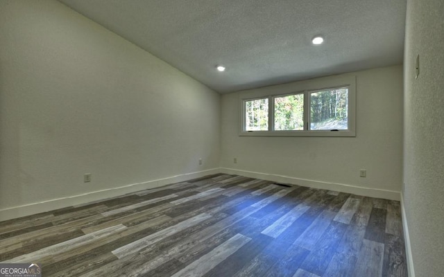 spare room featuring dark hardwood / wood-style floors, a textured ceiling, and vaulted ceiling