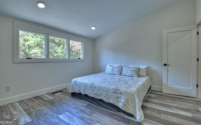 bedroom with lofted ceiling, wood-type flooring, and a textured ceiling