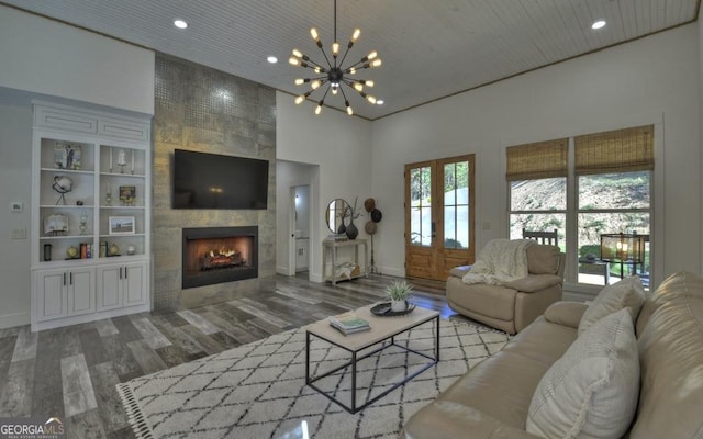 living room with a tile fireplace, a high ceiling, built in features, a notable chandelier, and hardwood / wood-style floors