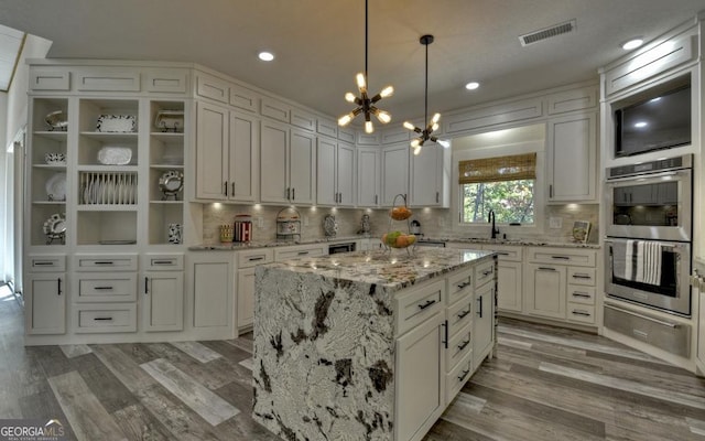 kitchen with double oven, a kitchen island, a chandelier, and wood-type flooring