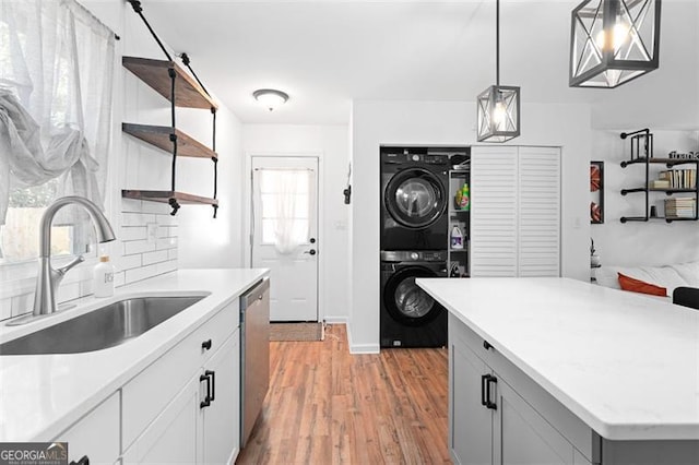 kitchen featuring dishwasher, sink, hanging light fixtures, light hardwood / wood-style flooring, and stacked washing maching and dryer