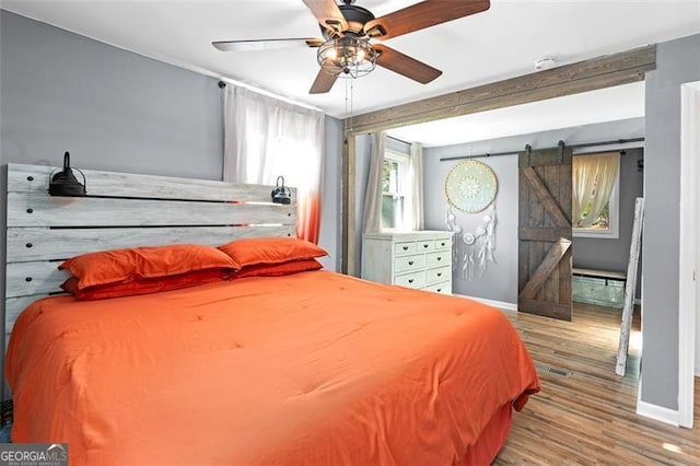 bedroom with a barn door, ceiling fan, and light wood-type flooring