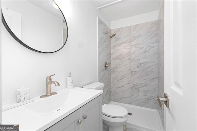 bathroom featuring a tile shower, vanity, and toilet