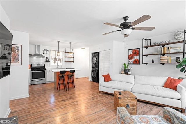 living room with light wood-type flooring, stacked washer and dryer, and ceiling fan