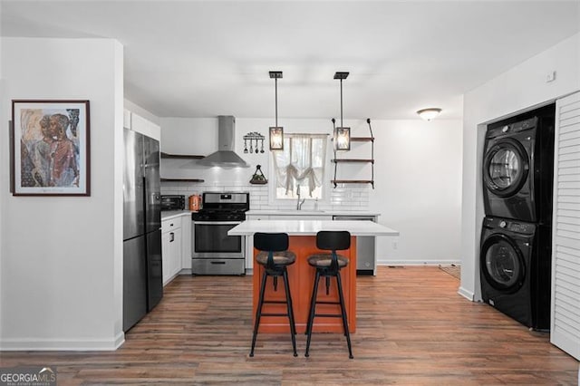 kitchen featuring white cabinets, black fridge, wall chimney exhaust hood, stainless steel range, and stacked washer / dryer