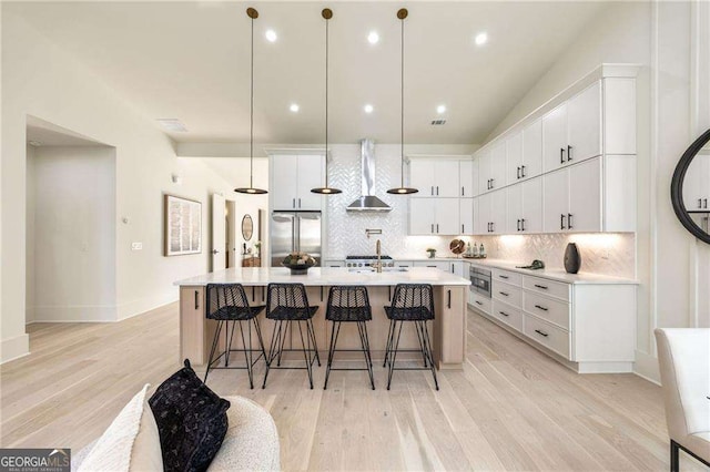 kitchen with white cabinets, stainless steel appliances, wall chimney exhaust hood, and an island with sink