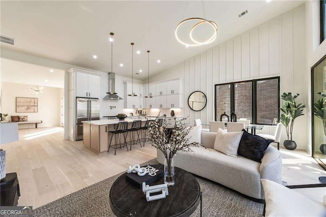 living room featuring high vaulted ceiling, light hardwood / wood-style floors, and an inviting chandelier