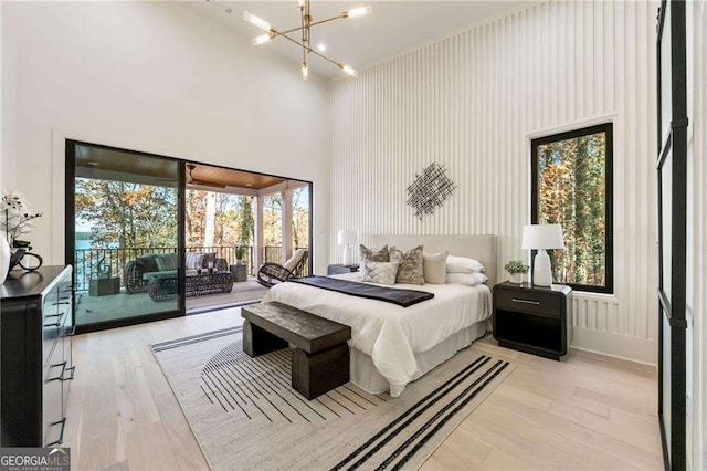 bedroom with access to exterior, a towering ceiling, multiple windows, and light wood-type flooring