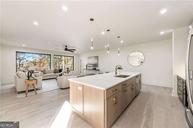 kitchen featuring ceiling fan, sink, decorative light fixtures, a kitchen island with sink, and light wood-type flooring