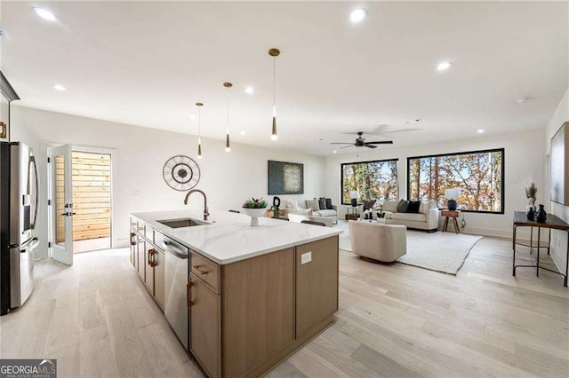 kitchen featuring a center island with sink, sink, appliances with stainless steel finishes, decorative light fixtures, and light hardwood / wood-style floors