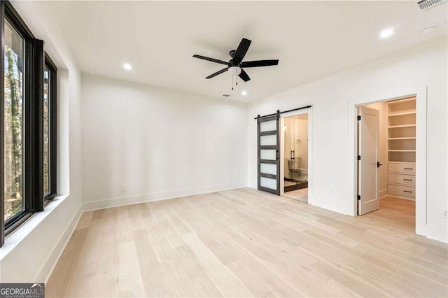 empty room featuring a barn door, light hardwood / wood-style floors, and ceiling fan