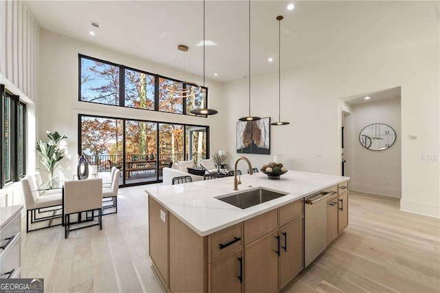 kitchen with dishwasher, sink, an island with sink, pendant lighting, and light hardwood / wood-style floors