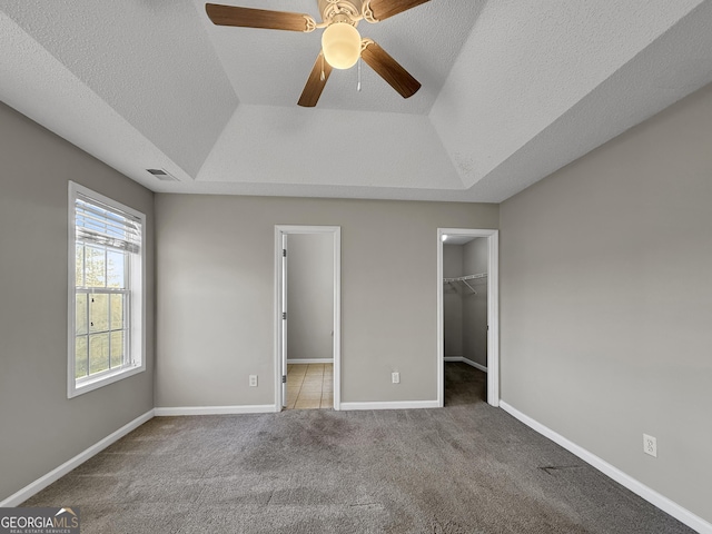 unfurnished bedroom featuring a textured ceiling, a walk in closet, carpet floors, and ceiling fan