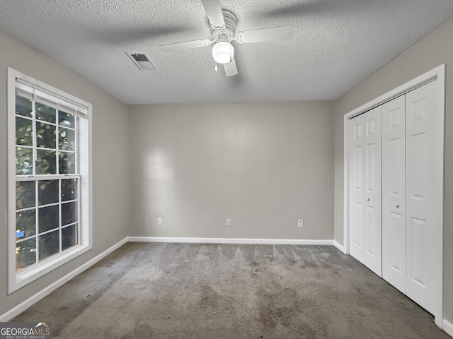 unfurnished bedroom featuring ceiling fan, dark carpet, a textured ceiling, and a closet