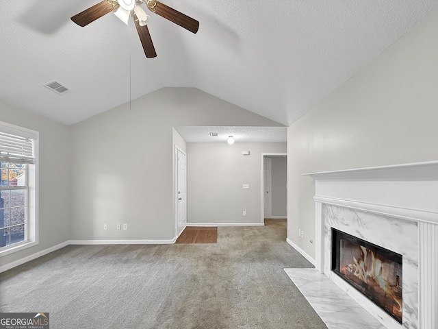 unfurnished living room with light carpet, a textured ceiling, vaulted ceiling, ceiling fan, and a fireplace