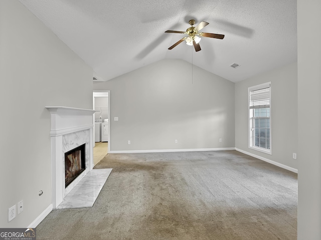 unfurnished living room featuring lofted ceiling, ceiling fan, washer and dryer, a premium fireplace, and light colored carpet