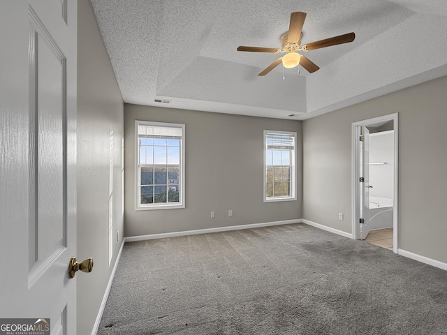 carpeted spare room featuring a raised ceiling, ceiling fan, and a textured ceiling