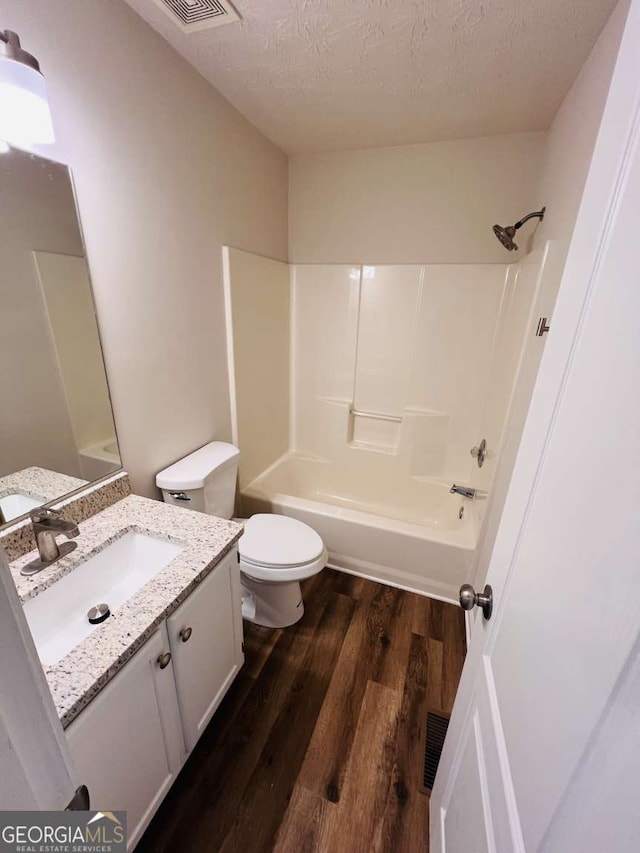 full bathroom featuring vanity, a textured ceiling, shower / bathing tub combination, hardwood / wood-style floors, and toilet