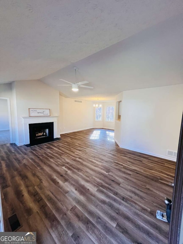 unfurnished living room featuring a textured ceiling, ceiling fan with notable chandelier, vaulted ceiling, and dark wood-type flooring