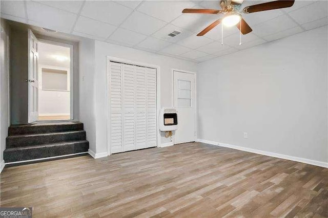 unfurnished bedroom featuring wood-type flooring, a paneled ceiling, heating unit, and ceiling fan