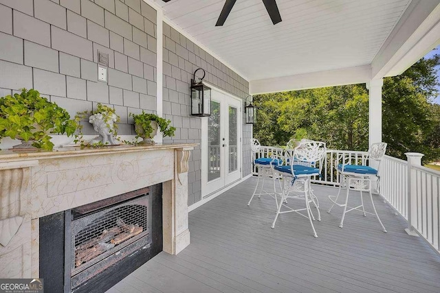 wooden deck with ceiling fan, covered porch, a tiled fireplace, and french doors